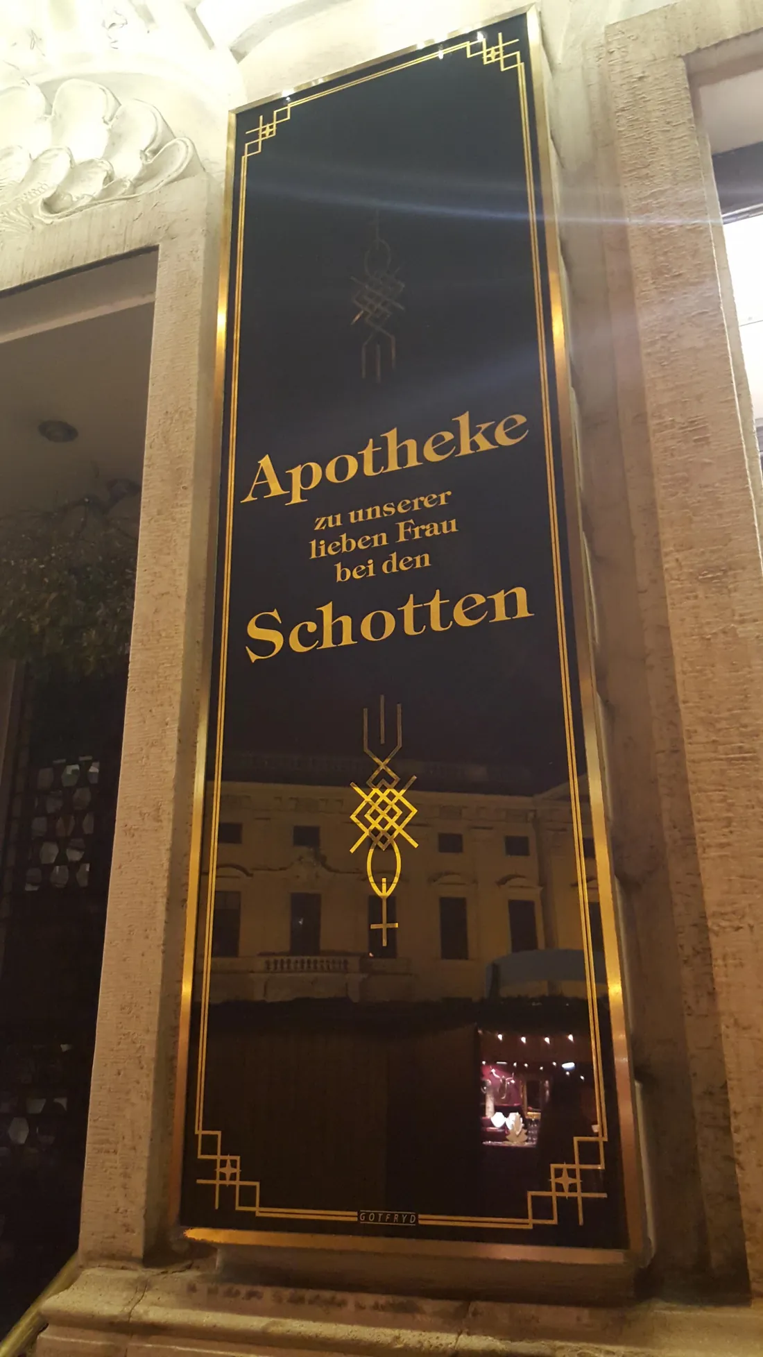 Schwarzes Glasschild mit Goldschrift „Apotheke zu unserer lieben Frau bei den Schotten“ und Art-déco-Ornamenten am Eingang