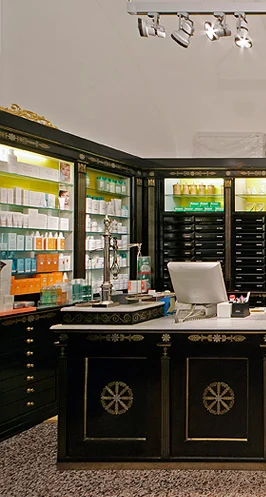 Offizin der Schottenapotheke: schwarze, vergoldete Schubladenschränke, darüber ein Marienbild mit Uhr, davor eine Vitrine mit Teesäckchen